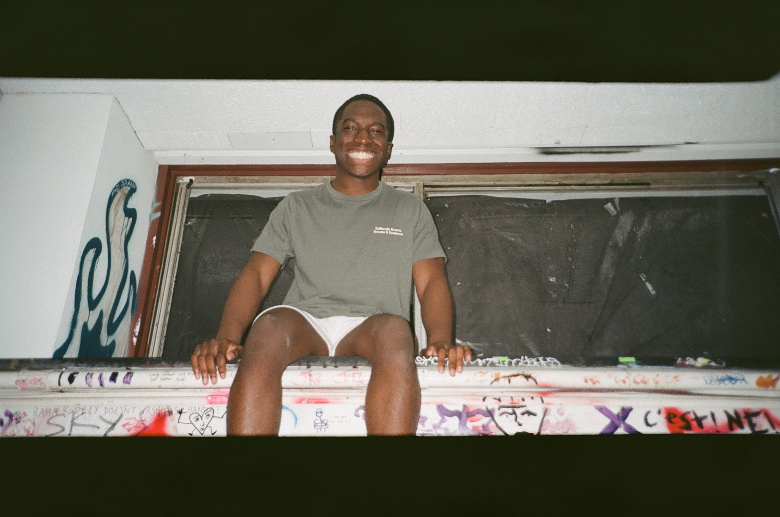 A smiling person sitting in a graffiti-covered window frame
